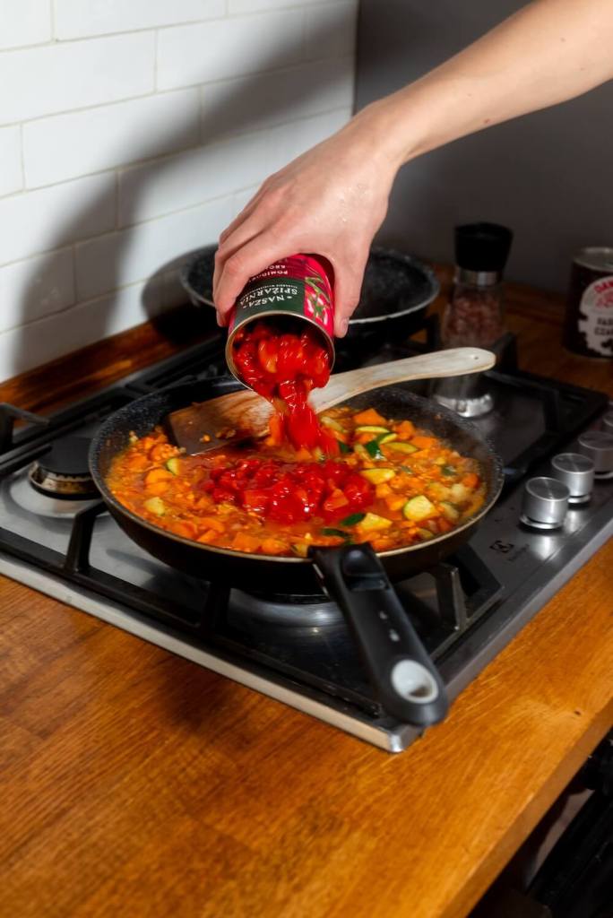 chef hand pouring tomatoes on a pan